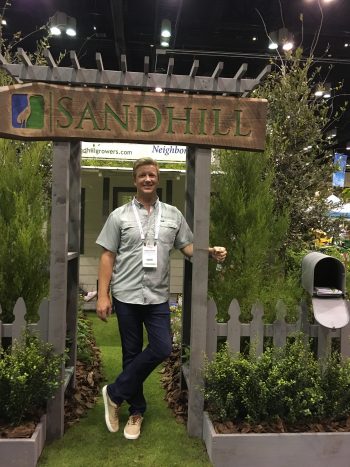 Chris Holly, Sandhill Growers & Environmental Services, stands at the entry to his booth, featuring a beautiful gray picket fence and porch surrounded by native plants.